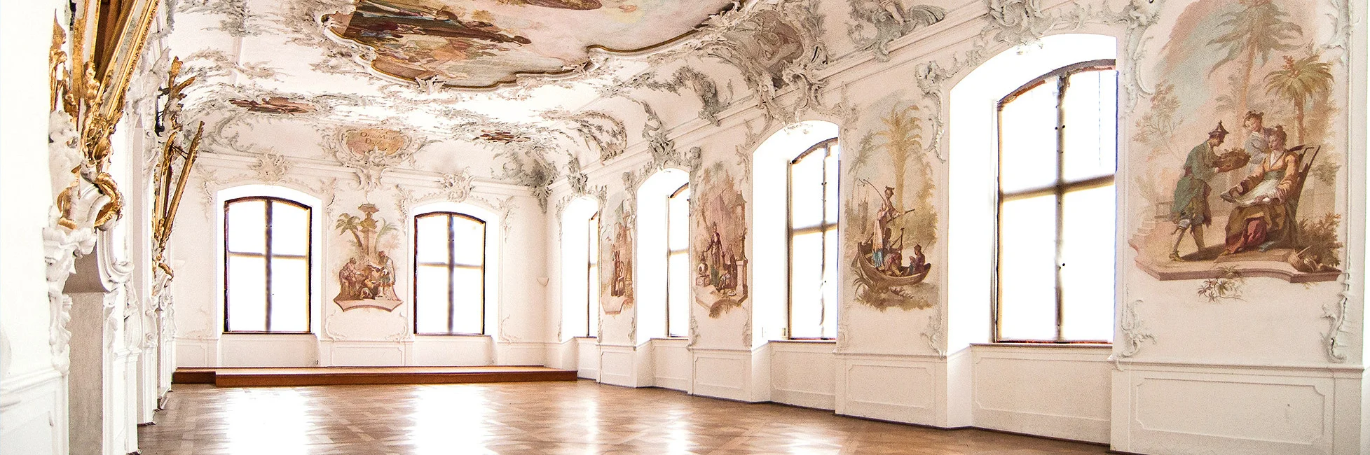 Schloss Leitheim Großer heller Raum mit Stuckdecke, Deckengemälde und großen Fenstern an der rechten Wand.